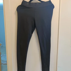Svarta leggings från Puma - Svarta leggings från Puma med bred resår i midjan där PUMA-loggan är diskret invävd. Snygg, tight passform och stretchigt material som sitter skönt mot kroppen. Perfekta för träning eller chill, och funkar lika bra till hoodie som till crop top.