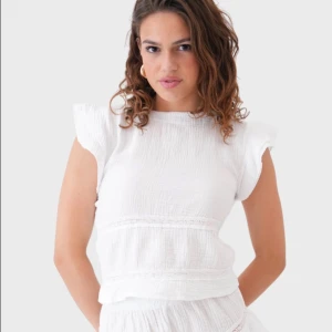 Vit blus med volangärmar i storleken XXS/XS💕 - Säljer en söt vit blus i bomull med volangärmar och fina spetsdetaljer. Blusen har en luftig och lätt struktur, rund halsringning och är perfekt för varma dagar. 💕