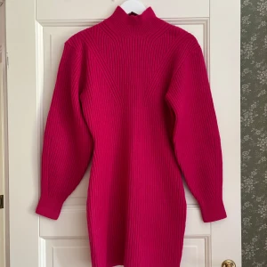 Rosa ribbad stickad klänning H&M - Superfin rosa stickad klänning från H&M med ribbad struktur och hög krage. Klänningen har långa ärmar och är i en kort modell, perfekt för lager på lager. Tillverkad av återvunnen polyester för en hållbar vibe.