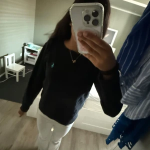 Svart stickad tröja från Polo Ralph Lauren - Svart stickad tröja från Polo Ralph Lauren i storlek S. Klassisk design med rund hals och lång ärm, samt den ikoniska turkosa Polo-loggan broderad på bröstet. Perfekt för dig som gillar stilrena och tidlösa plagg med en touch av lyx.