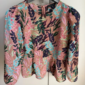 Blommig blus från Stockh LM, strl 36 - Superfin blus från Stockh LM i storlek 36 med färgglatt blommönster i lila, turkos, rosa och grönt på en beige botten. Modellen har långa ärmar, rund hals och dragkedja bak. Perfekt för dig som gillar statement-plagg med mycket färg och mönster.