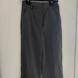 Grå kostymbyxor från Bik Bok - Stilrena grå kostymbyxor från Bik Bok i klassisk rak modell. Byxorna har hällor för bälte, diskreta fickor och stängs med dragkedja och knapp. Perfekta för en clean och dressad look. Materialet känns mjukt och följsamt.