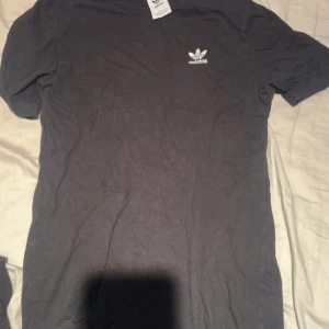 Svart Adidas t-shirt med logga - Svart t-shirt från Adidas med klassisk vit treklöver-logga på bröstet. Enkel och stilren design med rund hals och korta ärmar. Fint skick! 