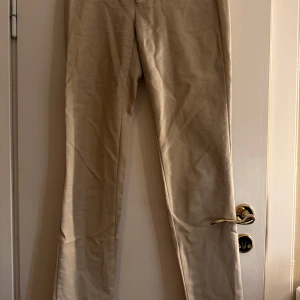 Beiga chinos från Calvin Klein - Snygga beiga chinos från Calvin Klein med klassisk rak passform. Byxorna har diskreta fickor och hällor för bälte. Perfekta för en clean och stilren look. Materialet är mjukt och känns skönt mot huden.
