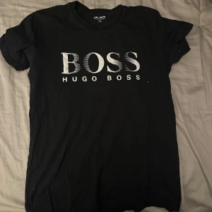 Svart t-shirt från Hugo Boss XS - Svart t-shirt från Hugo Boss i klassisk modell med rund hals och korta ärmar. Stor vit BOSS-logga framtill som ger en clean och stilren vibe. Skön bomullskänsla och passar perfekt till jeans eller shorts.sällsynt tröja