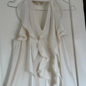 Vit volangblus från Zara - Supersöt vit blus från Zara med volangdetaljer längs framsidan och ärmlös design. Blusen har v-ringning och är i storlek xs