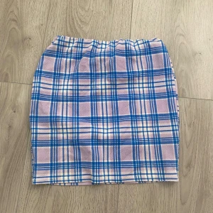 Rutig kortkjol från Boohoo - Säljer en söt rutig kortkjol från Boohoo i pastellfärger. Kjolen har en rak passform och elastisk midja. Mönstret är blått, lila och vitt, vilket ger en fräsch och ungdomlig vibe. Perfekt att matcha med en enkel topp och sneakers.