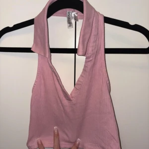 Rosa ribbad linnetopp från H&M - Säljer en ljusrosa croppad linnetopp från H&M i storlek S. Toppen har en bred krage och djup v-ringning, är ribbad och ärmlös vilket ger en chill och trendig vibe. Perfekt för dig som gillar att sticka ut med färg och coola detaljer.