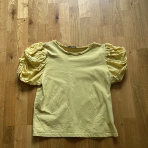 Jättefin gul topp ifrån zara - Supersnygg gul topp ifrån Zara med puffärm, perfekt för både skola och festliga outfits. Puffärmarna ger en lyxig detalj till tröjan. Den är i bra skick och i storlek S