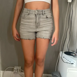 Grå jeansshorts från Denim Rebel - Snygga grå jeansshorts från Denim Rebel i högmidjad modell. De har råa, fransiga benslut och klassiska femficksdetaljer. Perfekta för sommarens alla äventyr och ger en cool vibe till din outfit.