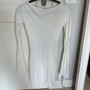 Vit kort klänning med öppen rygg - Supersnygg vit kort klänning med långa ärmar och öppen rygg som knyts med band i nacken. Klänningen har en tight passform och är tillverkad i ett mjukt material som sitter skönt på kroppen. 