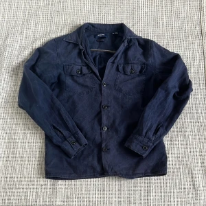 Jack & Jones overshirt - Snygg mörkblå overshirt från Jack & Jones med klassisk krage, två bröstfickor med knappar och långa ärmar. Skjortan är tillverkad i bomull och har en rak passform som funkar perfekt över en t-shirt. Stängs med knappar framtill.