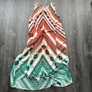 Mönstrad långklänning från ASOS - Snygg långklänning från ASOS med ärmlös design och coolt grafiskt mönster i orange, svart, vitt och turkost. Klänningen har rund halsringning och är tillverkad i ett lätt, flowy material som passar perfekt för varma dagar.man kan trä silkesband genom hålet för att få en midja. 34 men upp till 38 kan ha denna