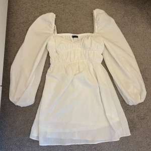 Vit kort klänning med puffärmar - Superfin vit kort klänning från bershka med puffiga långa ärmar. Säljer den då den är för liten och inte kommer till användning längre. Endast använd ett fåtal gånger. 
