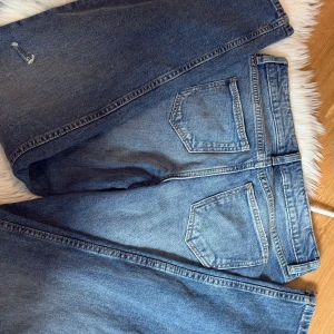 Raka jeans  -  jeans i mellanblå tvätt med raka ben och normal passform. Jeansen har fem fickor, knappgylf och slitna detaljer på benen för en cool, avslappnad look. Perfekta för dig som gillar tidlös denimstil.