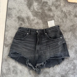 Svarta jeansshorts med fransig kant - Snygga svarta jeansshorts med fransig kant nertill. Shortsen har slitna detaljer framtill och klassisk femficksdesign. Perfekta för en avslappnad och trendig look under sommaren. Väldigt små i storleken skulle säga att de passar 34. Aldrig använda