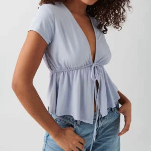 Ljuslila omlottopp med knyt - Supersöt ljuslila topp med v-ringning och knyt framtill. Modellen har korta ärmar och en flowy, lite croppad passform som ger en avslappnad vibe. Perfekt att styla med jeans eller kjol för en trendig look.