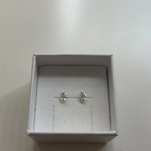 Silverfärgade droppformade örhängen - Snygga små örhängen i silverfärg med droppformad design och glittrande stenar. Perfekta för att ge en elegant touch till din stil. Kommer i en vit ask.