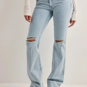 Ljusblå bootcut jeans med slitningar - Snygga ljusblå jeans med bootcut passform och slitna hål på båda knäna. Jeansen har klassisk femficksdesign och coola broderade detaljer på bakfickorna. Perfekta för en avslappnad och trendig look.