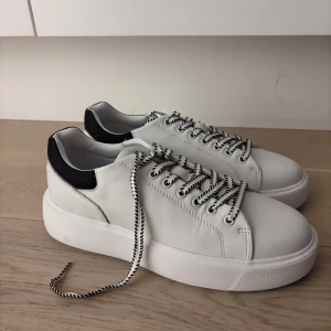 Vita sneakers från Philip Hog - Stilrena vita sneakers från Philip Hog med svart detalj vid hälen och coola svartvita snören. Skorna har en chunky platt sula och är gjorda i skinn för en clean look. 