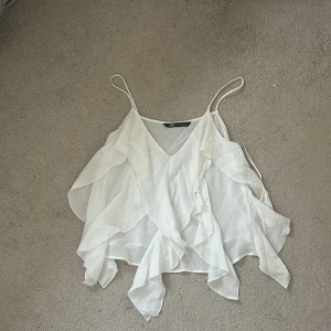 Vit volangig linnetopp från Zara - Supersöt vit linnetopp från Zara med tunna axelband och v-ringning. Toppen har flera lager av volanger som ger en flowy och luftig känsla. Perfekt för varma dagar men även bara fin för andra tillfällen