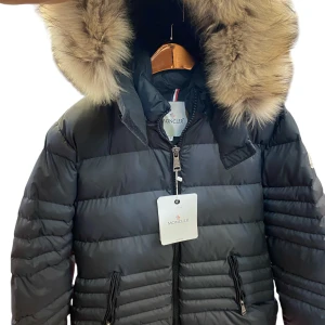 Svart  dunjacka med pälshuva - Snygg svart dunjacka  med fluffig pälskant på huvan. Jackan har quiltad design, dragkedja framtill och två fickor med dragkedja. Perfekt för kalla dagar när du vill vara både varm och stilren.