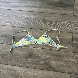 Färgglad bikiniöverdel  - Snygg bikiniöverdel i triangelform. Mönstret är en mix av blått, gult och svart med inslag av vitt, vilket ger en fräsch och somrig vibe. Perfekt för stranden eller poolen.