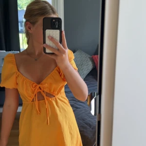 Gul kort klänning med snörning - Superfin gul kort klänning med puffärmar och snygg snörning framtill. Klänningen har en cut-out detalj under bysten och är gjord i ett lätt, somrigt tyg. Perfekt för varma dagar