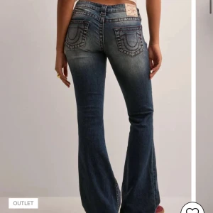 Blå bootcut jeans med  vinröda sömmar - Snygga blå jeans från True Religion med bootcut-passform och låg midja. Jeansen har markerade kontrastsömmar, klassiska bakfickor med broderad logga och en lätt tvättad look. Perfekta för dig som gillar en retro vibe och vill sticka ut. Slutsålda. Nypris ca 1300. Pris kan diskuteras