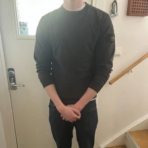 Svart sweatshirt från Stone Island - Säljer en svart sweatshirt från Stone Island med klassisk logga på vänster ärm. Tröjan har rund halsringning och långa ärmar med ribbade muddar. Perfekt för dig som gillar stilrena och snygga plagg med streetkänsla.