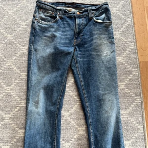 Blå jeans från Nudie Jeans, W32 L32 - Säljer ett par klassiska blå jeans från Nudie Jeans i modellen THIN FINN W32 L32. Jeansen har snyggt slitna detaljer, och kontrastsömmar. De har en rak passform och är tillverkade i mjukt bomullsjeans-tyg. Perfekta för en avslappnad och stilren look. Hör av er vid frågor eller funderingar ✅