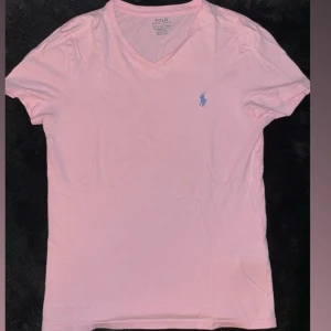 Rosa v-ringad t-shirt Polo Ralph Lauren - Ljusrosa t-shirt från Polo Ralph Lauren med v-ringning och blå broderad logga på bröstet. Modellen är slim fit och har korta ärmar. Tillverkad i mjuk bomull, perfekt för en clean och stilren look. Nypris 999 kr 