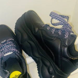 Buffalo London  svarta chunky sneakers - Buffalo sneakers i svart skinnimitation i stl 36  med riktigt chunky plattformssula (8cm) Skorna har svarta och vita snören med mönster och rund tå. Säljes då dem är för stora för mig. Enbart använda 2 gånger! Obs - skickas ej. Möts enbart  upp i Stockholms området. 