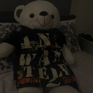 Svart t-shirt med stor tryckt text - Cool svart t-shirt med stor vit tryckt text och färgglada grafiska detaljer. T-shirten har korta ärmar och en klassisk passform. Perfekt för dig som gillar statement-plagg och vill sticka ut med en unik look.