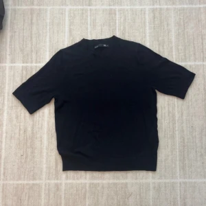 Svart kortärmad stickad tröja - En stilren svart stickad tröja med korta ärmar och rund hals. Tröjan har en enkel och clean design som passar perfekt till jeans eller kjol. Materialet känns mjukt och bekvämt mot huden, och den har en något loose passform.