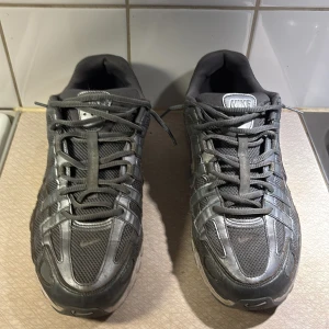 Nike P-6000 grå sneakers - Nike P-6000 sneakers i helgrå färg med mesh och syntetpaneler. Skorna har en sportig vibe med tydliga linjer, snörning och en chunky sula. Perfekta för dig som gillar retrostil och streetwear. Swoosh-logga på sidan och bekväm vadderad insida.