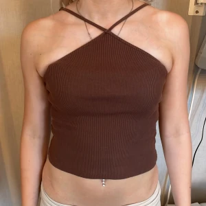 Brun ribbad croppad topp BikBok XS - Säljer en brun croppad ribbad topp från BikBok i storlek XS. Toppen har smala axelband som korsas framtill och ger en snygg detalj vid halsen. Perfekt till jeans eller kjol för en trendig look.