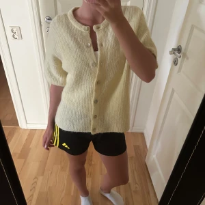 Gul kofta i ullmix från Gina Tricot - Supermysig ljusgul kofta från Gina Tricot i ullblandning. Koftan har korta ärmar, rund halsringning och knäpps med knappar framtill. Perfekt för lager-på-lager och ger en chill vibe till din outfit.