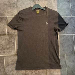 Ralph lauren T-shirt  - Snygg mörkgrå t-shirt från Polo Ralph Lauren. Modellen är slim fit och sitter perfekt om du har runt st S. Väldigt fint skick eftersom den nästan aldrig användes.