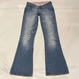 Låmidjade bootcut jeans med slitningar - Jätte snygga ljusblåa jeans med en del slitningar, säljer pga att de ej kommer till användning. Midja 37x2 cm , gren 17 cm och innerben 81cm💕 Obs svag rosa fläck på sista bilden.  Märkta som W27/L32 Bilder från förra ägare!!
