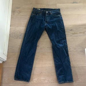 Levi's 501 blå jeans W30 L32 - Klassiska Levi's 501 jeans i mörkblå denim. Har aldrig använt dom och pris kan diskuteras. Rak passform med fem fickor och knappgylf. Snygga kontrastsömmar och ikonisk läderpatch bak i midjan. Perfekta för dig som gillar tidlös stil och premiumkänsla.