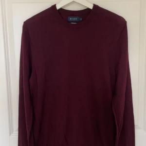 Vinröd tröja från Riley - Snygg vinröd långärmad tröja från Riley i klassisk modell. Tröjan har rund halsringning och är tillverkad i mjukt material som heter Merino wool. Perfekt för dig som gillar stilrena och enkla plagg med en modern touch. Nypris 799kr