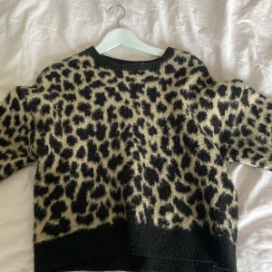 Leopardmönstrad stickad tröja NA-KD - Supermjuk stickad tröja från NA-KD med leopardmönster i svart och beige. Tröjan har rund halsringning, långa ärmar och ribbade muddar vid ärmslut och nederkant. Perfekt för dig som vill sticka ut med en trendig look.