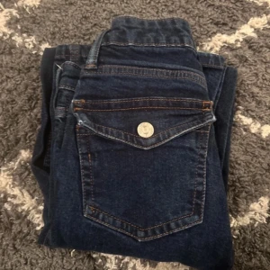 Mörkblå jeans från 157 med fickdetaljer - Snygga mörkblå jeans från 157 med klassiska kontrastsömmar och unika fickor med lock och knapp framtill. Jeansen har normal passform och är tillverkade i slitstarkt denimtyg. Perfekta för dig som gillar en stilren men ändå cool look.