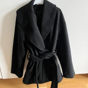 Svart kappa med bälte från Gina Tricot💕 - Stilren svart kappa från Gina Tricot i storlek XS. Jackan har bred krage, knyts med bälte i midjan och har långa ärmar. Perfekt för dig som gillar en klassisk look med modern touch. Materialet är mjukt och känns lyxigt. Den är lite nopprig men annars är den i väldigt bra skick. Priset kan diskuteras. Skriv om du undrar något. Ursprungligen köpt för 699 kr.💕