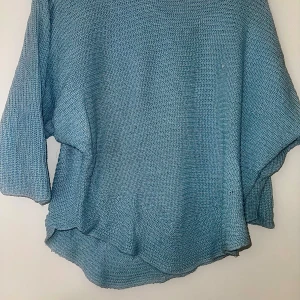 Skimrig stickad tröja Made in Italy - Ljusblå stickad tröja med loose passform och trekvartsärmar. Tröjan har en avslappnad siluett och är tillverkad i ett glansigt, stickat material som ger en cool textur. Bild 3: pytteliten fläck som går bort i tvätt.