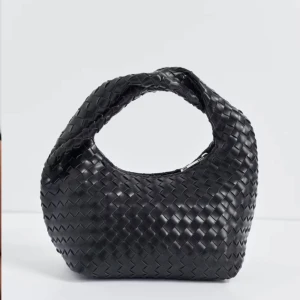 Svart flätad handväska i skinn - Snygg svart handväska med flätad design och rundad form. Väskan har ett kort handtag och är tillverkad i skinn, vilket ger en lyxig känsla. Perfekt accessoar för att lyfta din outfit med en trendig touch.