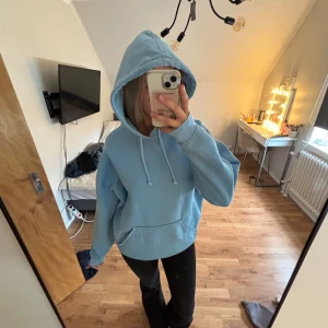 Ljusblå hoodie från BikBok - Mysig ljusblå hoodie från BikBok med huva och snörning. Tröjan har en klassisk känguruficka framtill och är i mjukt material med fleece på insidan. Perfekt för chill dagar eller när du vill vara extra comfy.