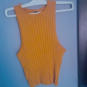 Ribbad croppad linnetopp i senapsgult från Divided - Säljer en ribbad croppad linnetopp i senapsgult från Divided. Toppen är ärmlös med rund halsringning och har en tight passform. Perfekt för varma dagar eller som ett lager under en skjorta och den är stretchig! 🤗