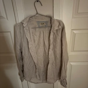Beige linneskjorta från East West - Säljer en beige skjorta i linne från East West. Skjortan har klassisk krage, långa ärmar och knäppning framtill. Perfekt för en avslappnad och stilren look. Perfekt nu till sommaren. Pris kan diskuteras.